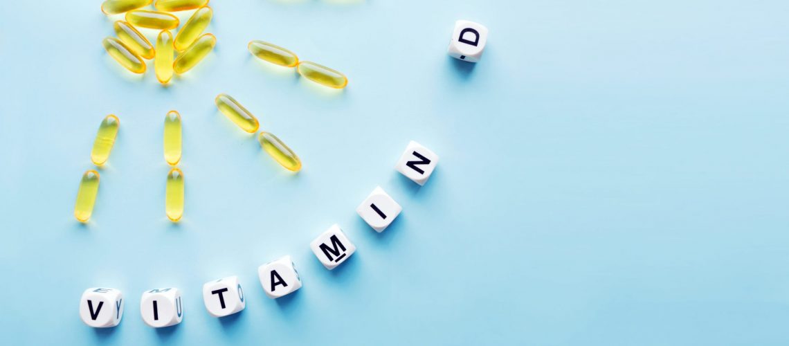 Yellow capsules in the form of the sun with rays and the word vitamin D from white cubes with letters on a blue background. VITAMIN D word for healthy and medical concept. Sunshine vitamin health benefits