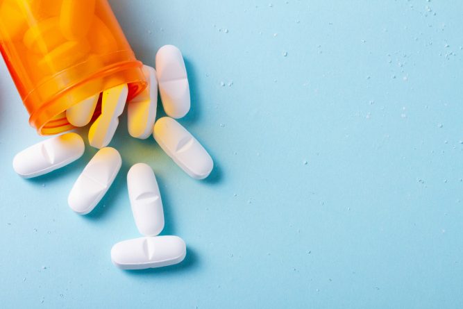 White pills in orange bottle on blue background close up with copy space