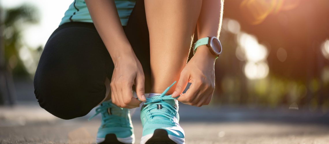 Running shoes - closeup of woman tying shoe laces. Female sport fitness runner getting ready for jogging in garden background.