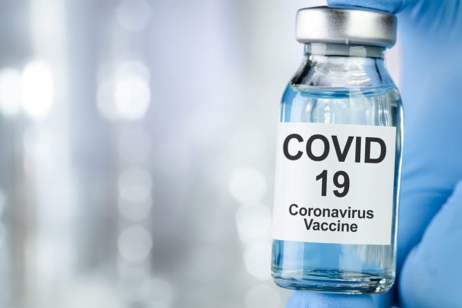 Healthcare cure concept with a hand in blue medical gloves holding Coronavirus, Covid 19 virus, vaccine vial