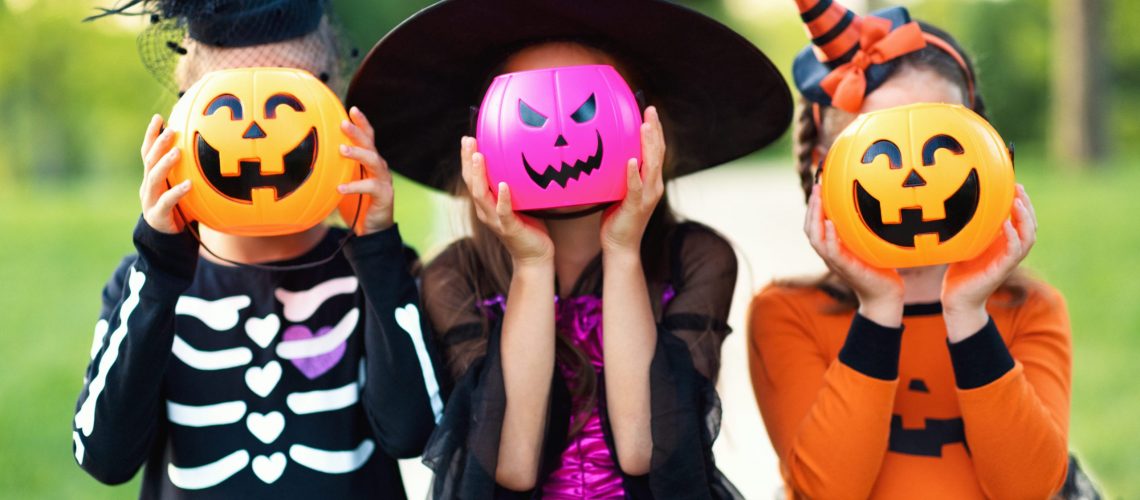 Happy Halloween! funny kids girls   in fancy dress hide their heads behind buckets pumpkins outdoors