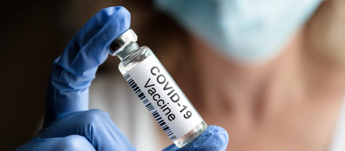 COVID-19 vaccine concept, female doctor holds coronavirus medication in office or laboratory. Bottle with vaccine for corona virus treatment closeup. Clinical trial due to coronavirus pandemic.
