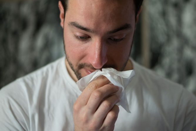 Man with tissue showing signs of allergies and possible fever