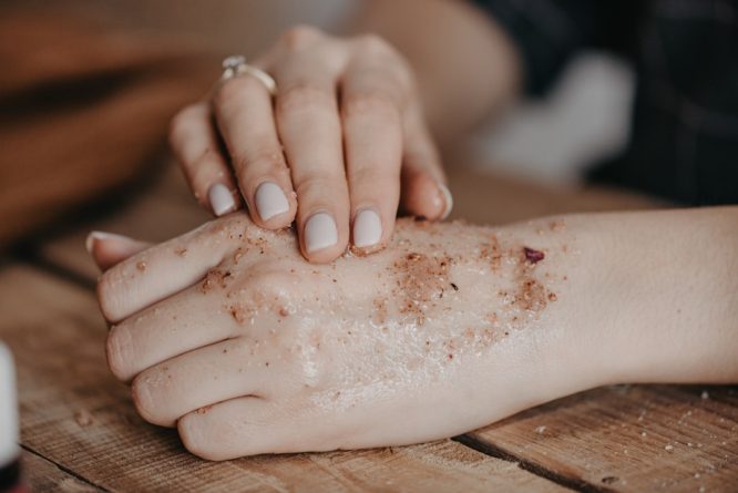 Hand with exfoliating scrub applied over skin lesions for skin care treatment