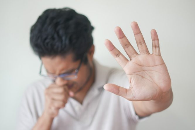 A man coughing from the flu, gesturing to stay back.
