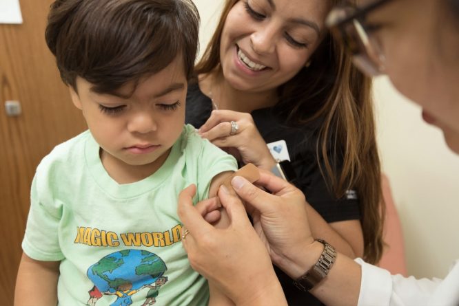 A young boy getting a measles shot with his mother at a doctor's office.